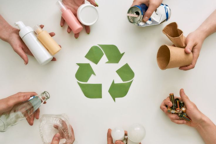 Hands holding various recyclable items around a green recycling symbol